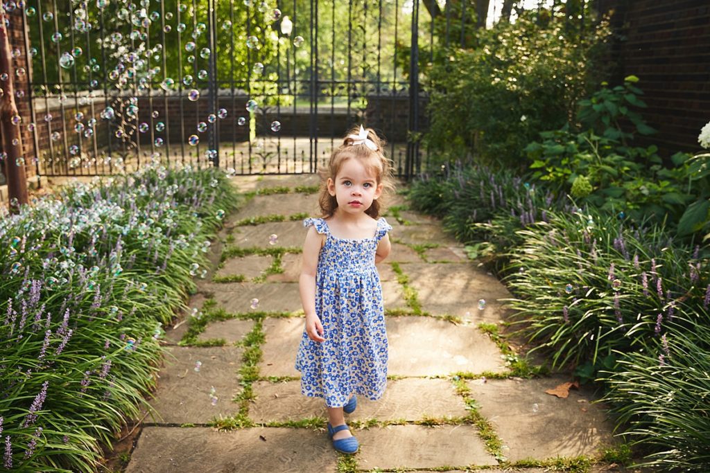 wexford little girl with bubbles during a photo session at the walled garden in Mellon Park with black metal gates and brick walls and flowers