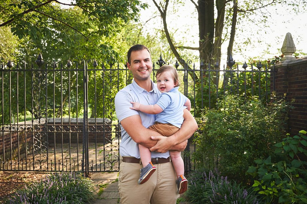 wexford dad holding son during a photo session at the walled garden in Mellon Park with black metal gates and brick walls and flowers