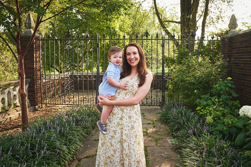 wexford mom holding son during a photo session at the walled garden in Mellon Park with black metal gates and brick walls and flowers
