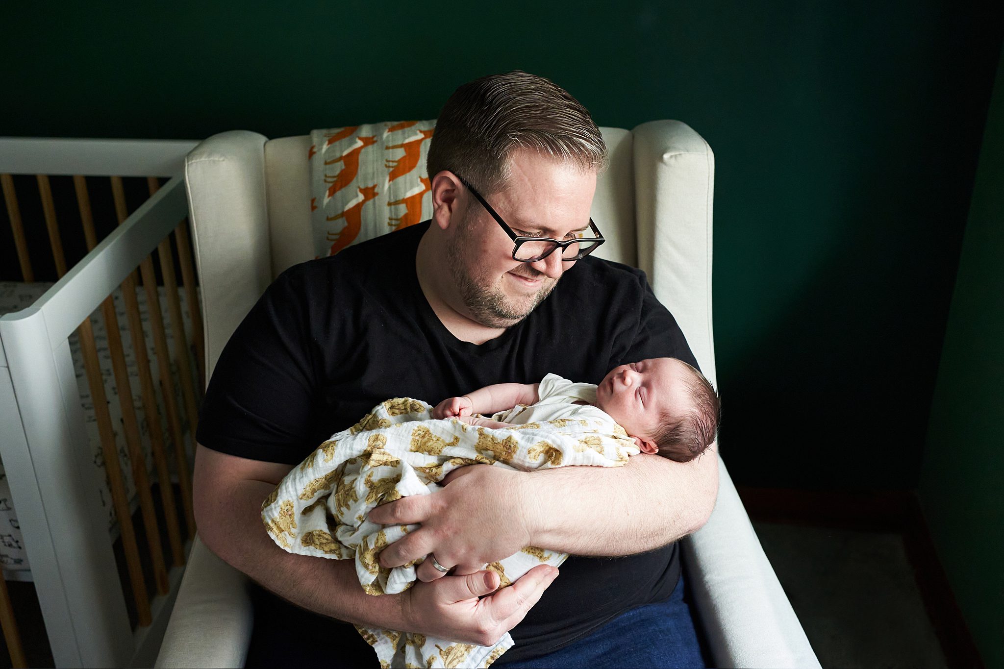 awake newborn baby with dad in rocking chair golden doodle blanket