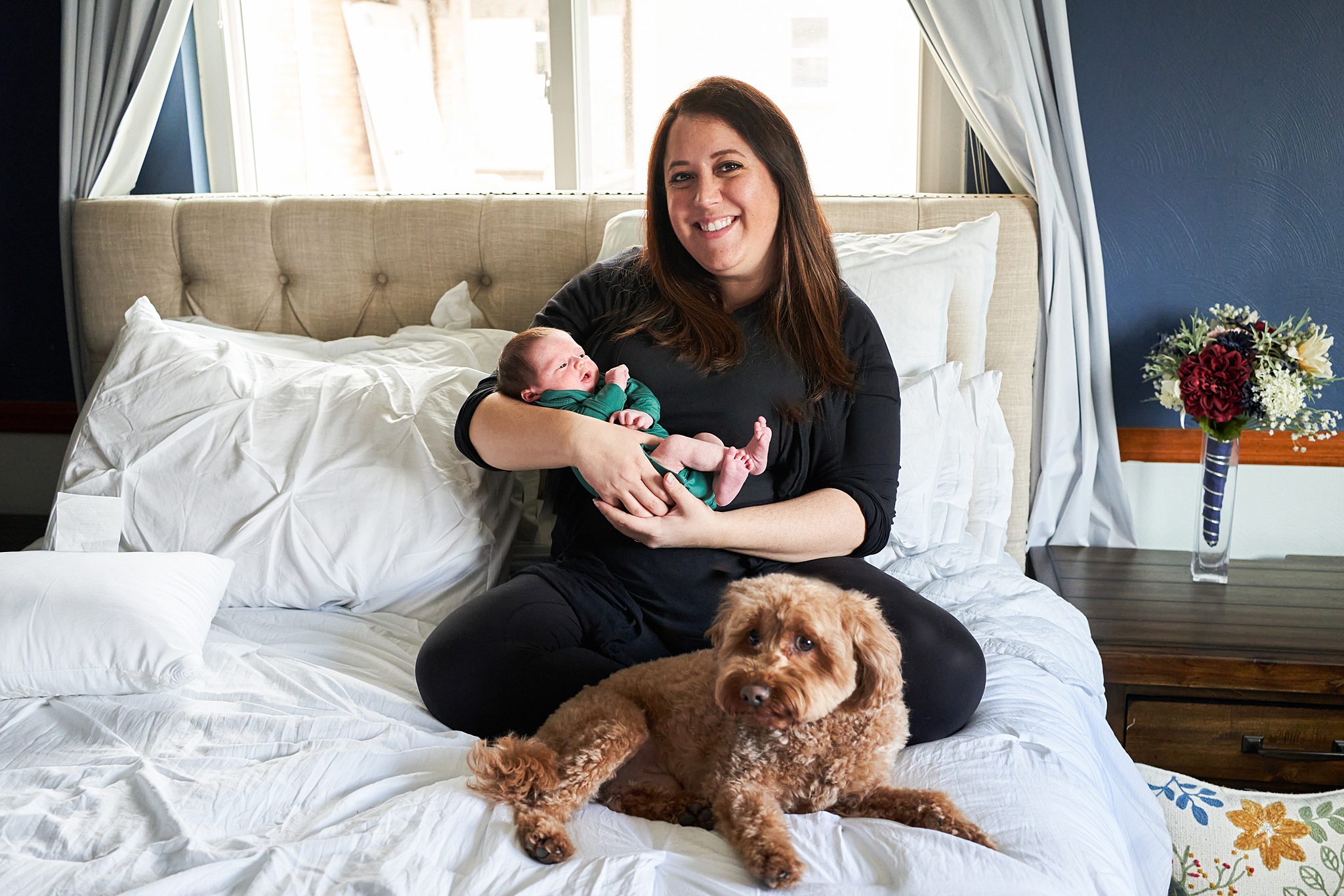 mom on bed with newborn in north hills home with golden doodle dog for a newborn photo session