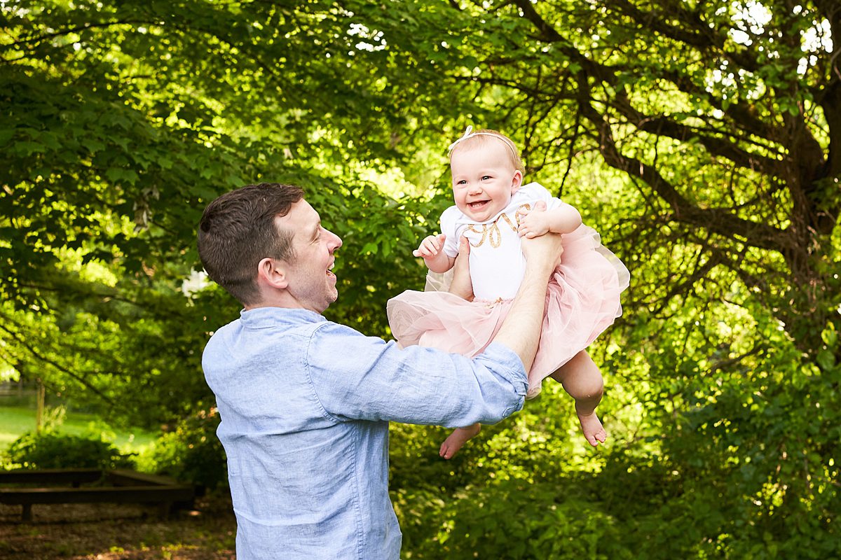dad holding up baby in first birthday outfit in beechwood park in fox chapel for a family photo session 