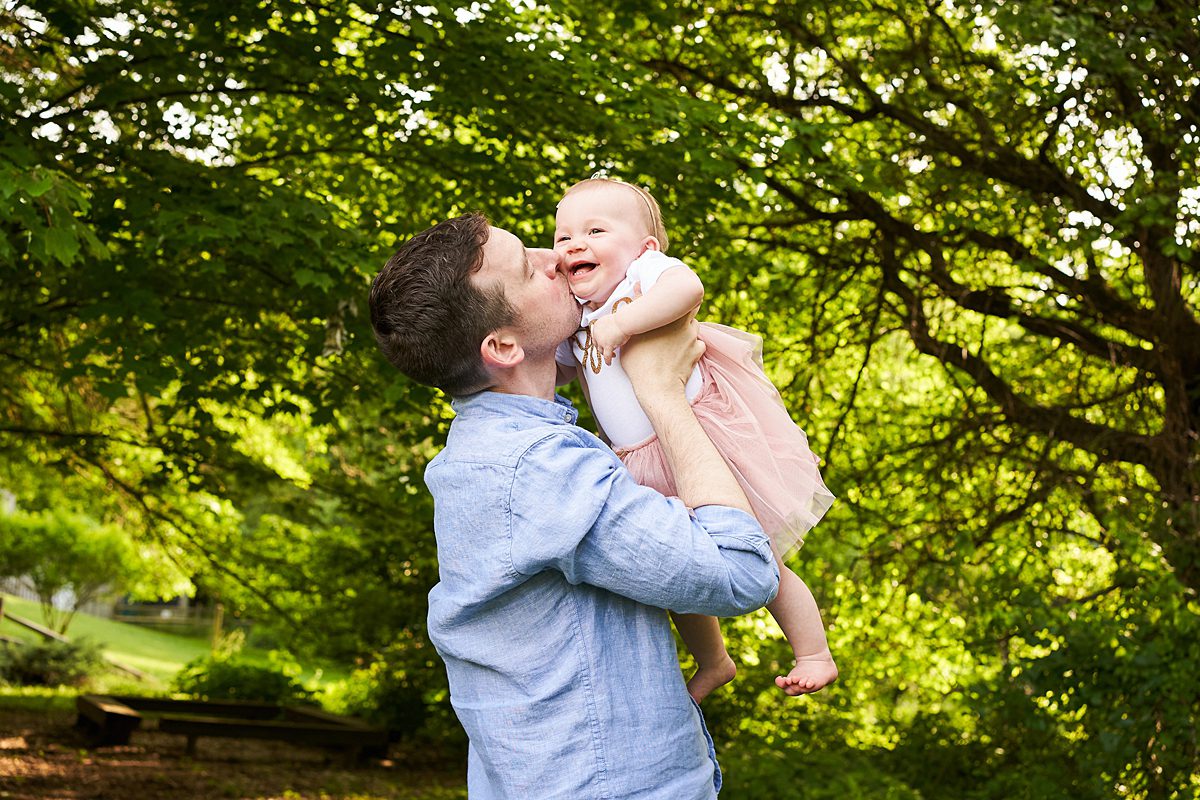 dad holding up and kissing baby in first birthday outfit in beechwood park in fox chapel for a family photo session 