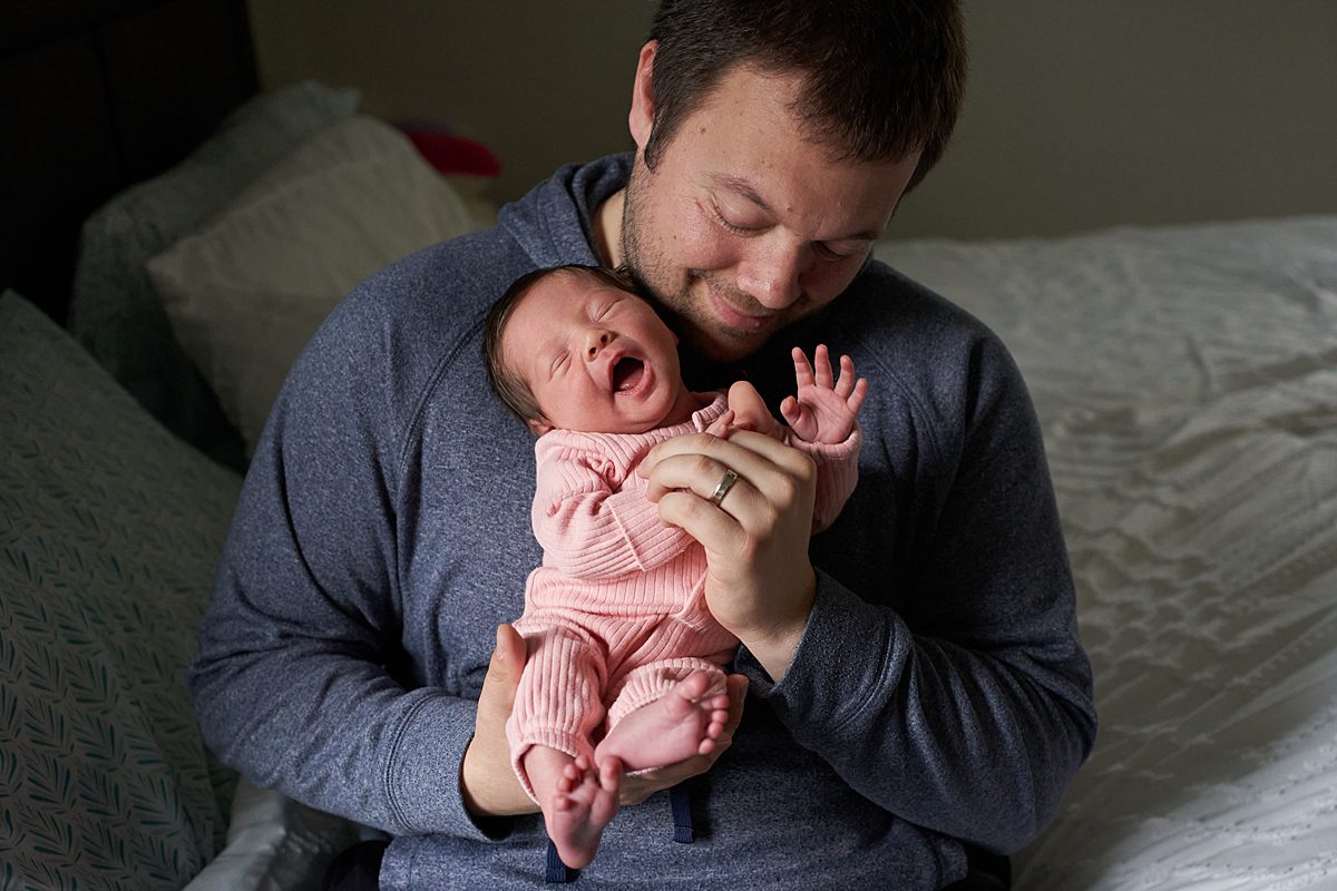 seven fields newborn photographer dad holding baby girl in pink sleeper