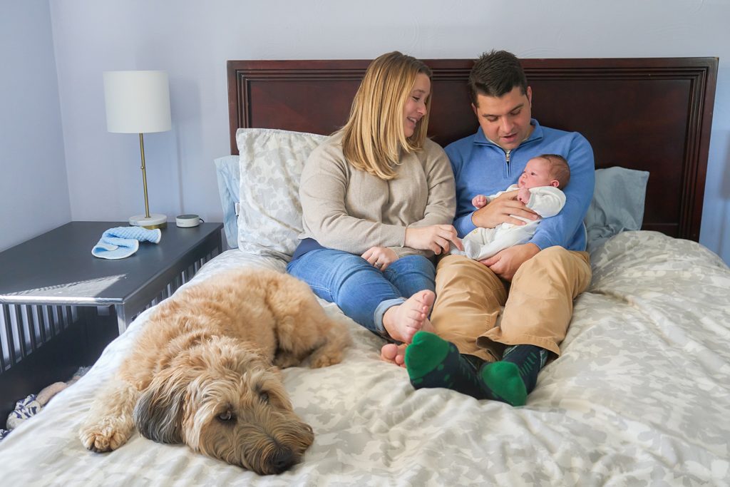 mom dad and newborn baby with dog on bed at mccandless area home