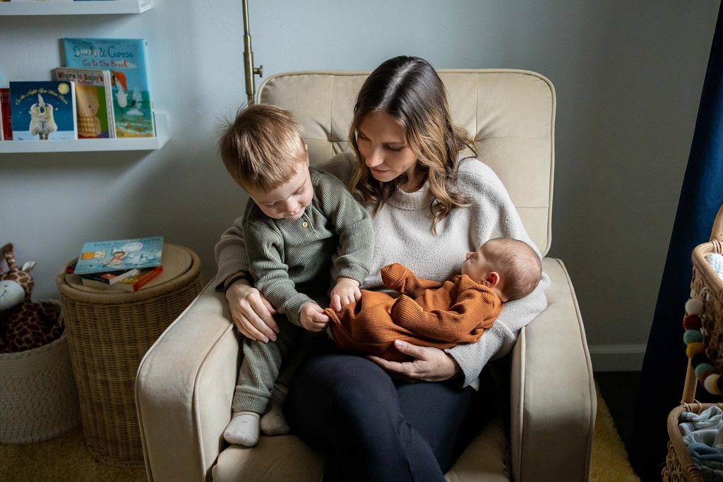 little boy toddler kissing newborn baby on rocking chair in boardman home