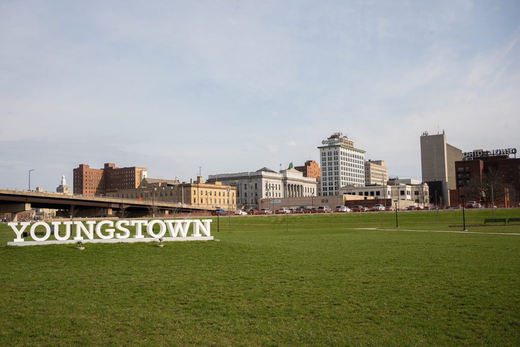 A grassy park in Mahoning County with a large "YOUNGSTOWN" sign stands before a city skyline of office and commercial buildings—one of the best locations for photo sessions in Youngstown.