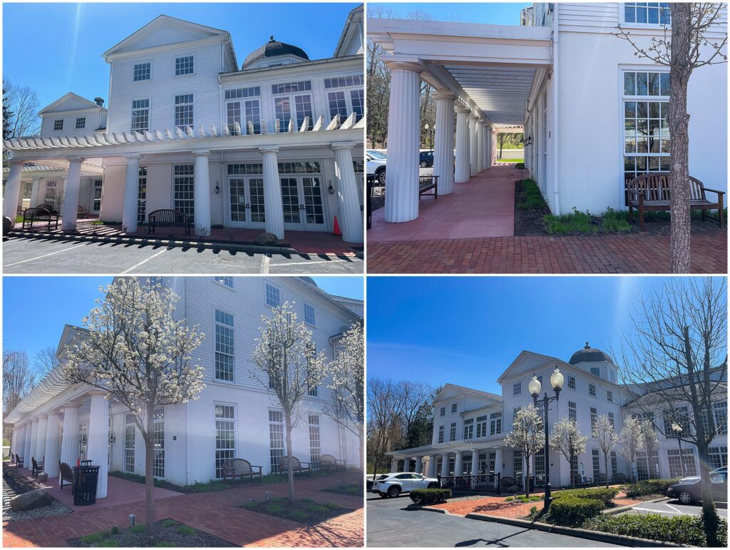 A white colonial-style building with pillars, large windows, blooming trees, benches, and a brick walkway on a sunny day—one of Mahoning County's top locations for photo sessions in Youngstown.