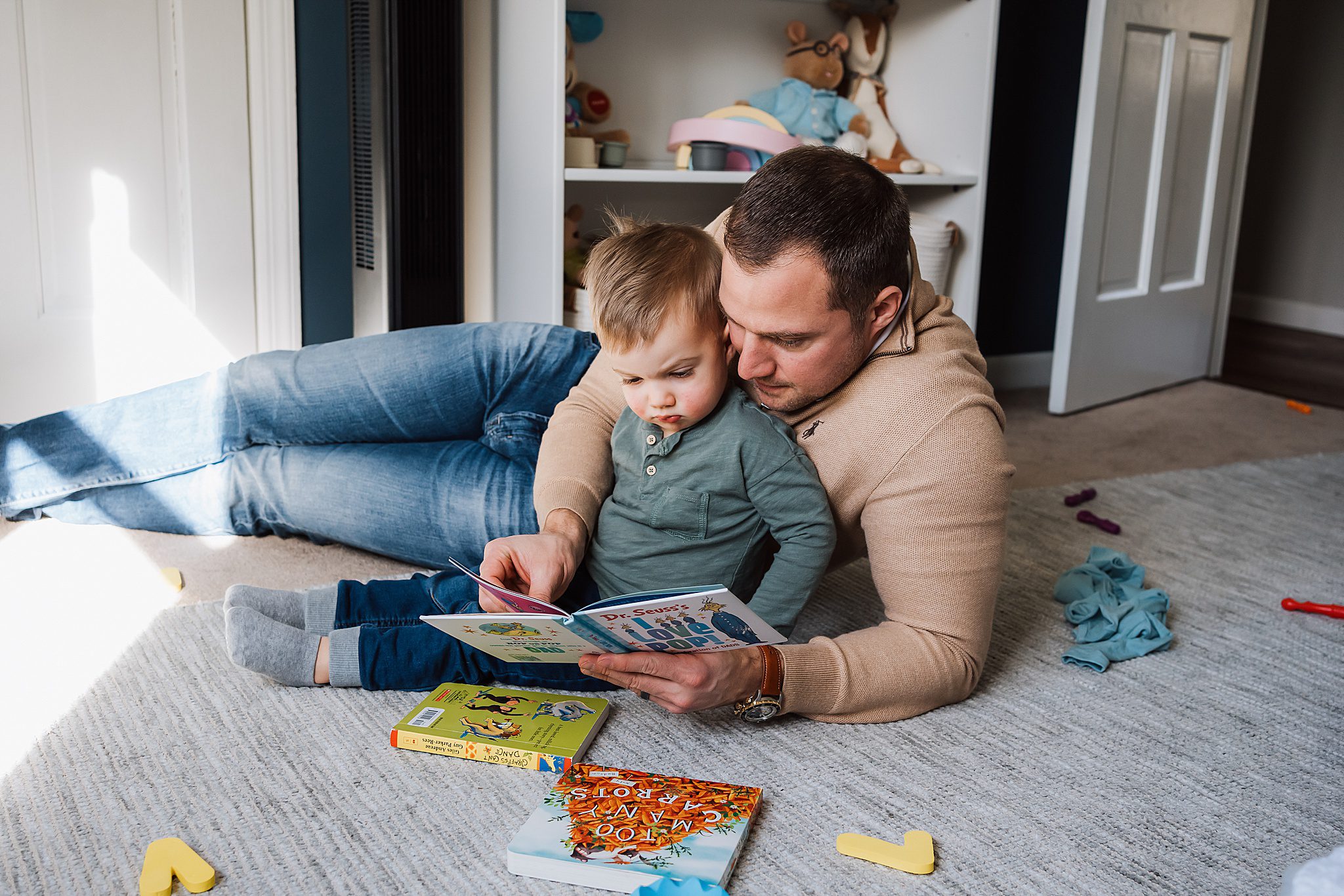 dad sitting on floor reading book to toddler son