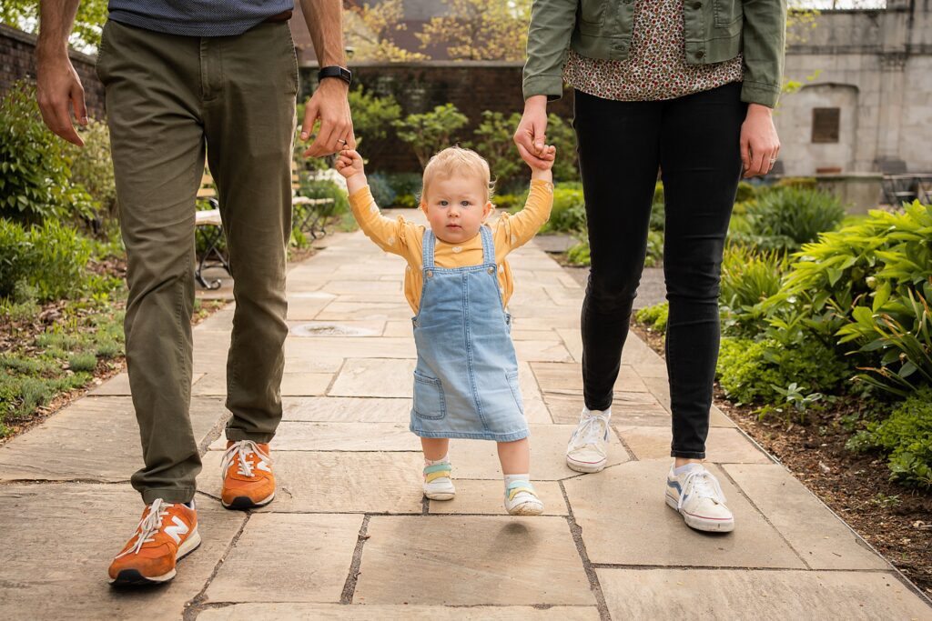 little girl holding hands with her parents walking in Mellon park walled garden SHADYSIDE