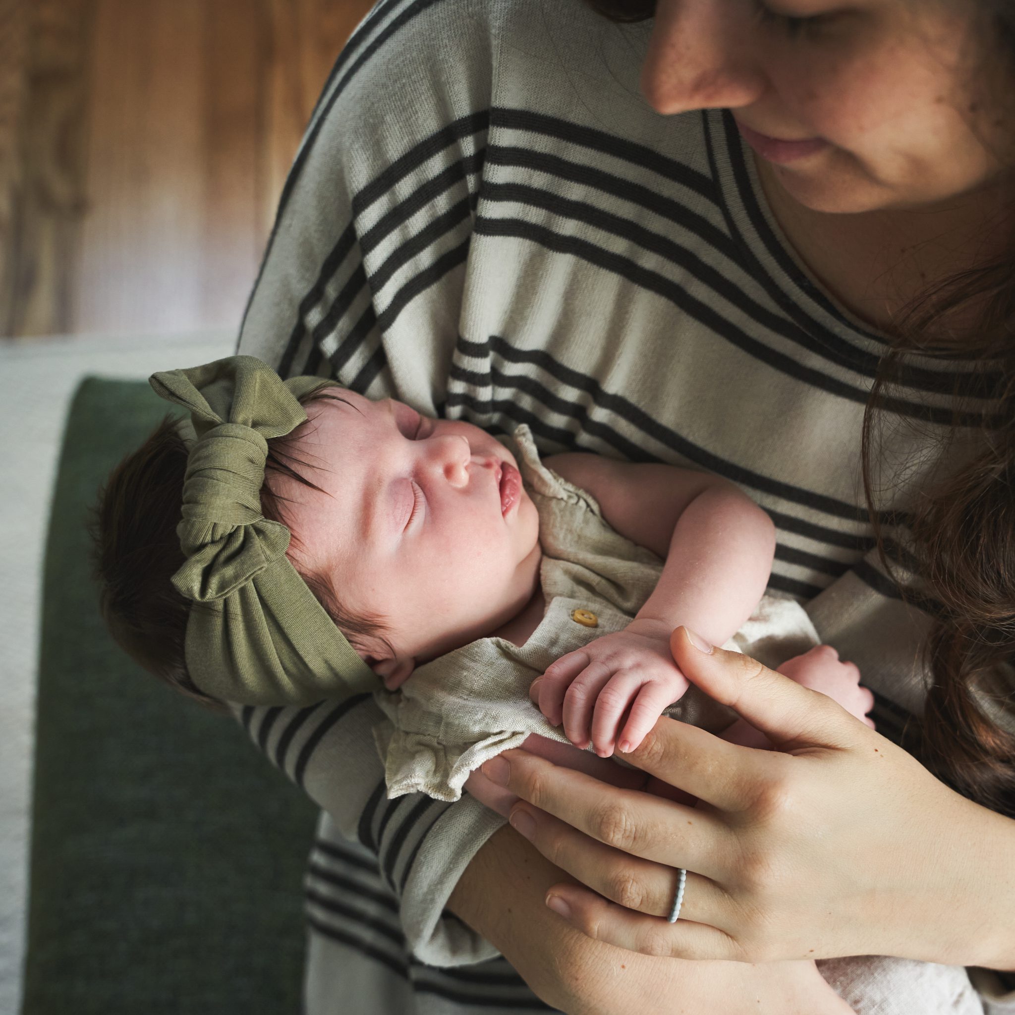 newborn baby with a green headband sleeping in moms arms in the window light