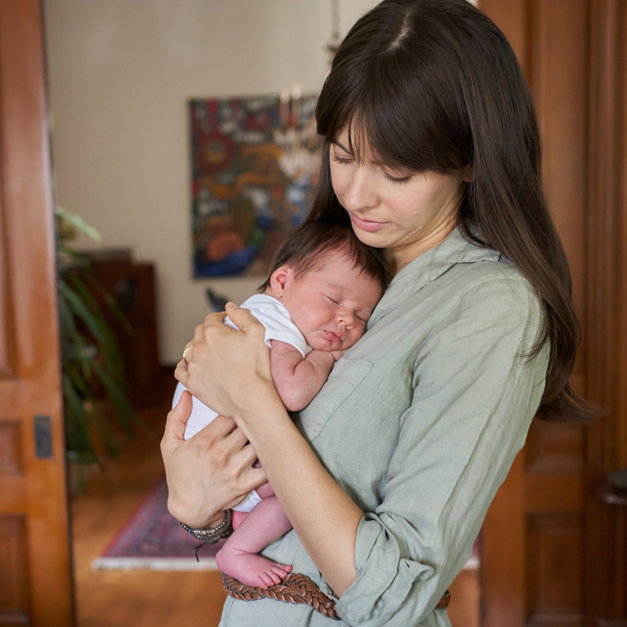 mom holding a sleeping newborn to her chest in home