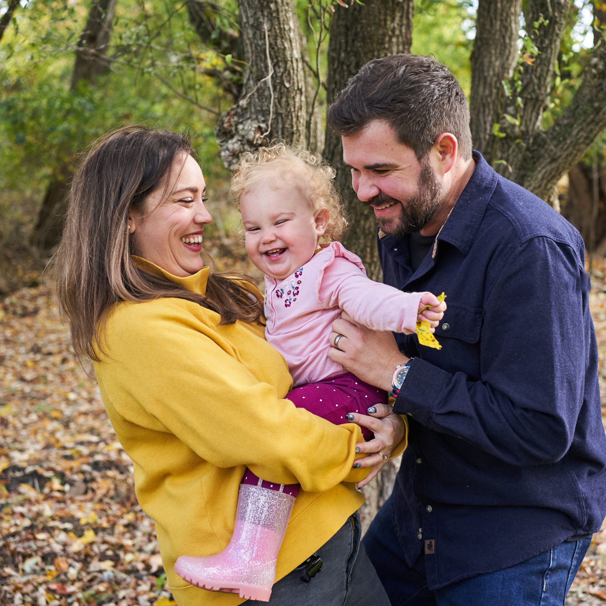mom and dad holding laughing toddler daughter in bright colors in the back yard