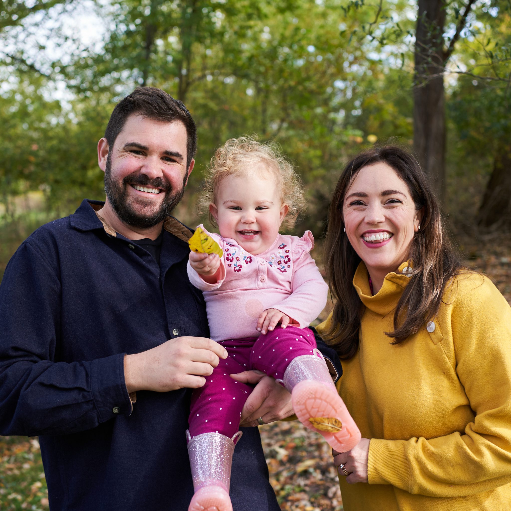 mom and dad holding toddler daughter in bright colors in the back yard