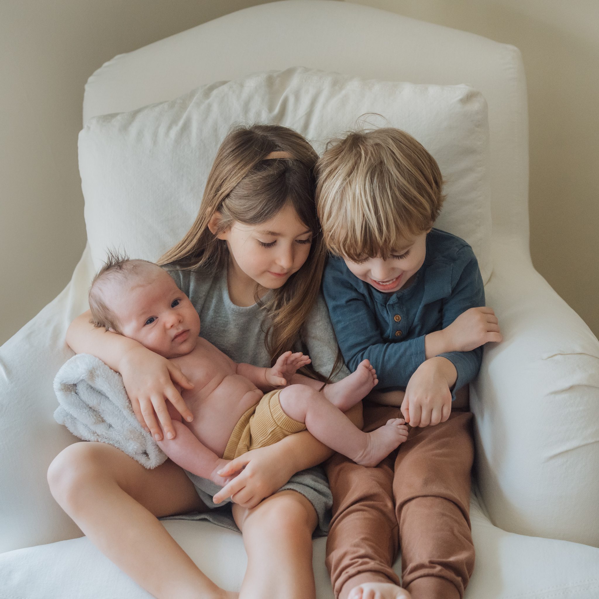 girl and brother holding their baby brother looking at his toes