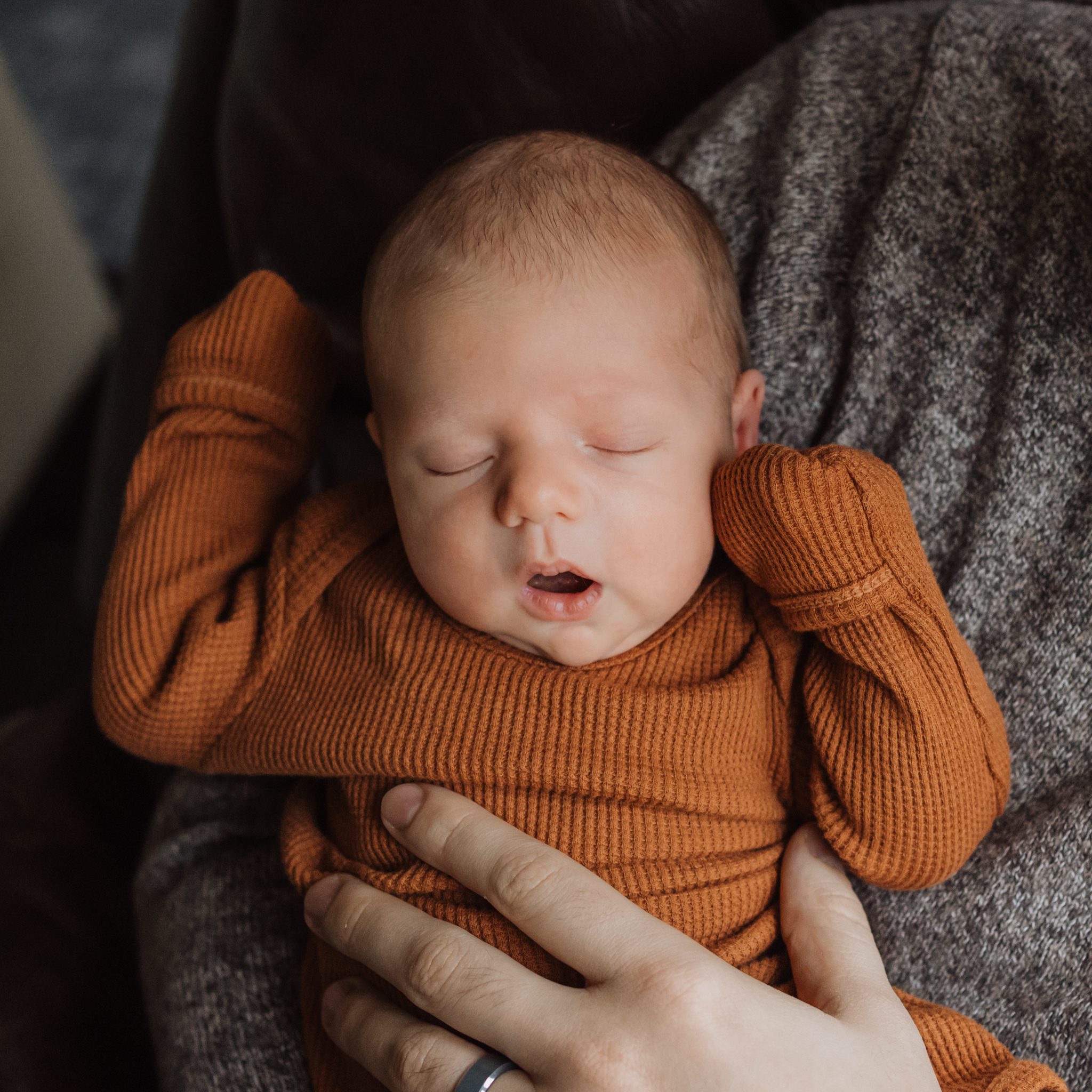 sleeping newborn with mouth open in dads arms by the window light