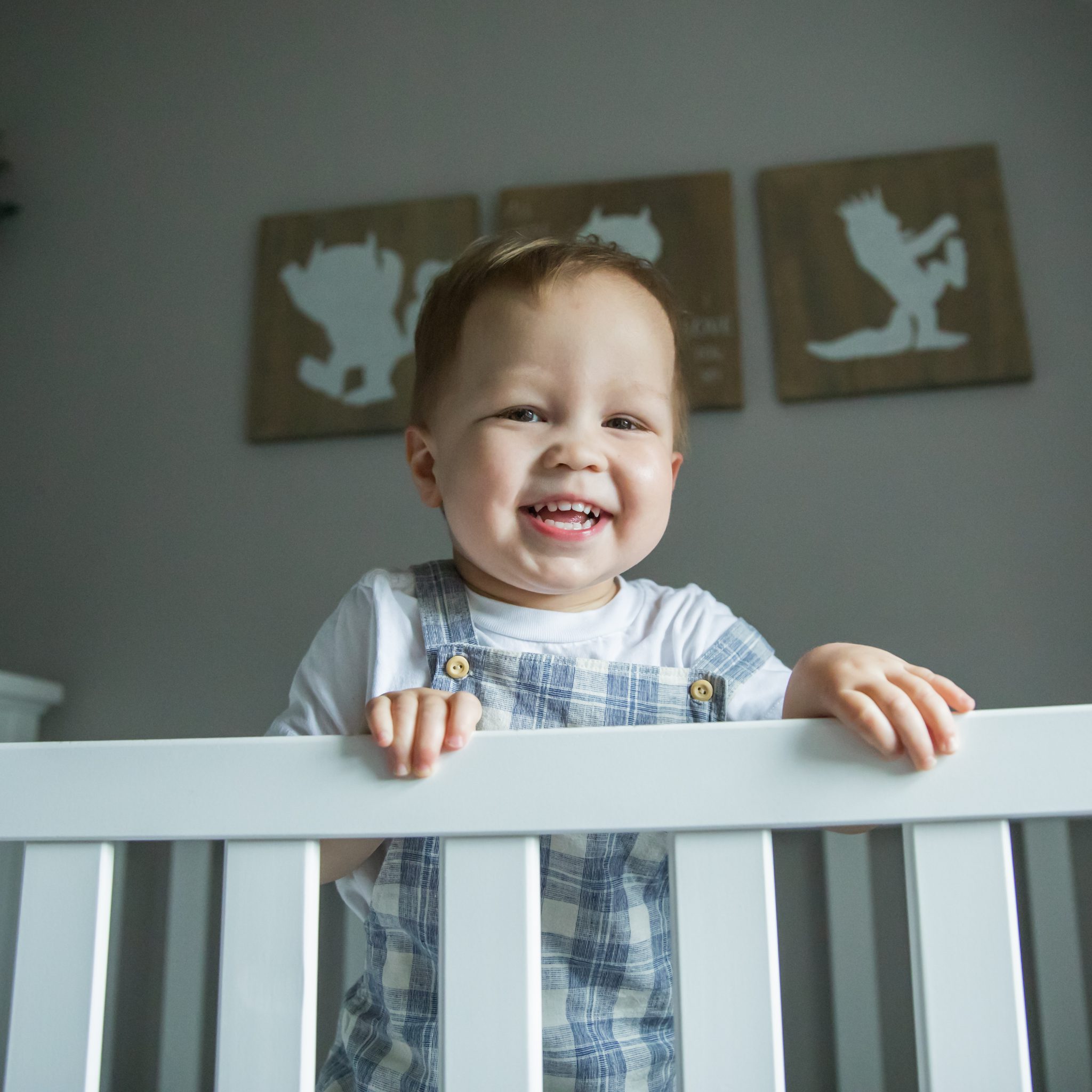 toddler standing in a white crib and smiling down at the camera