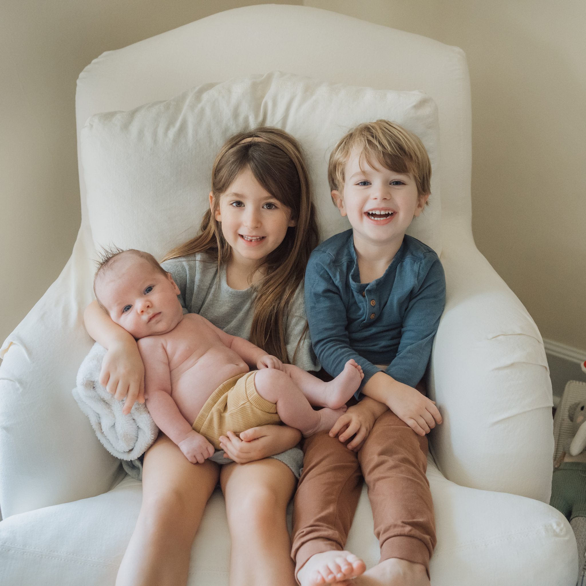 brother and sister holding their baby brother in a chair in the nursery
