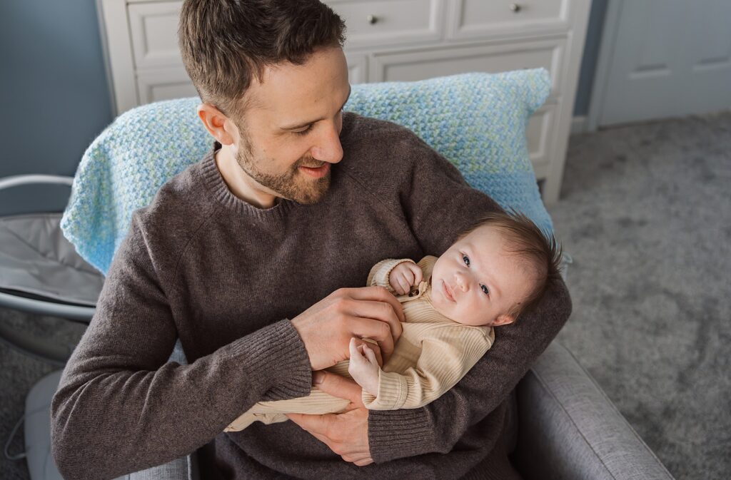 A smiling newborn photographer holding a baby in a cozy room.