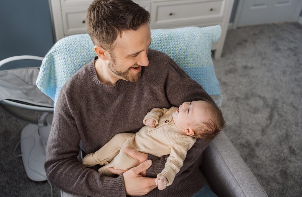 A smiling newborn photographer holding and looking affectionately at a baby in a cozy room.