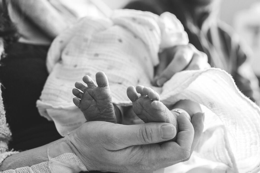 A black and white photo of a woman holding a baby's feet.
