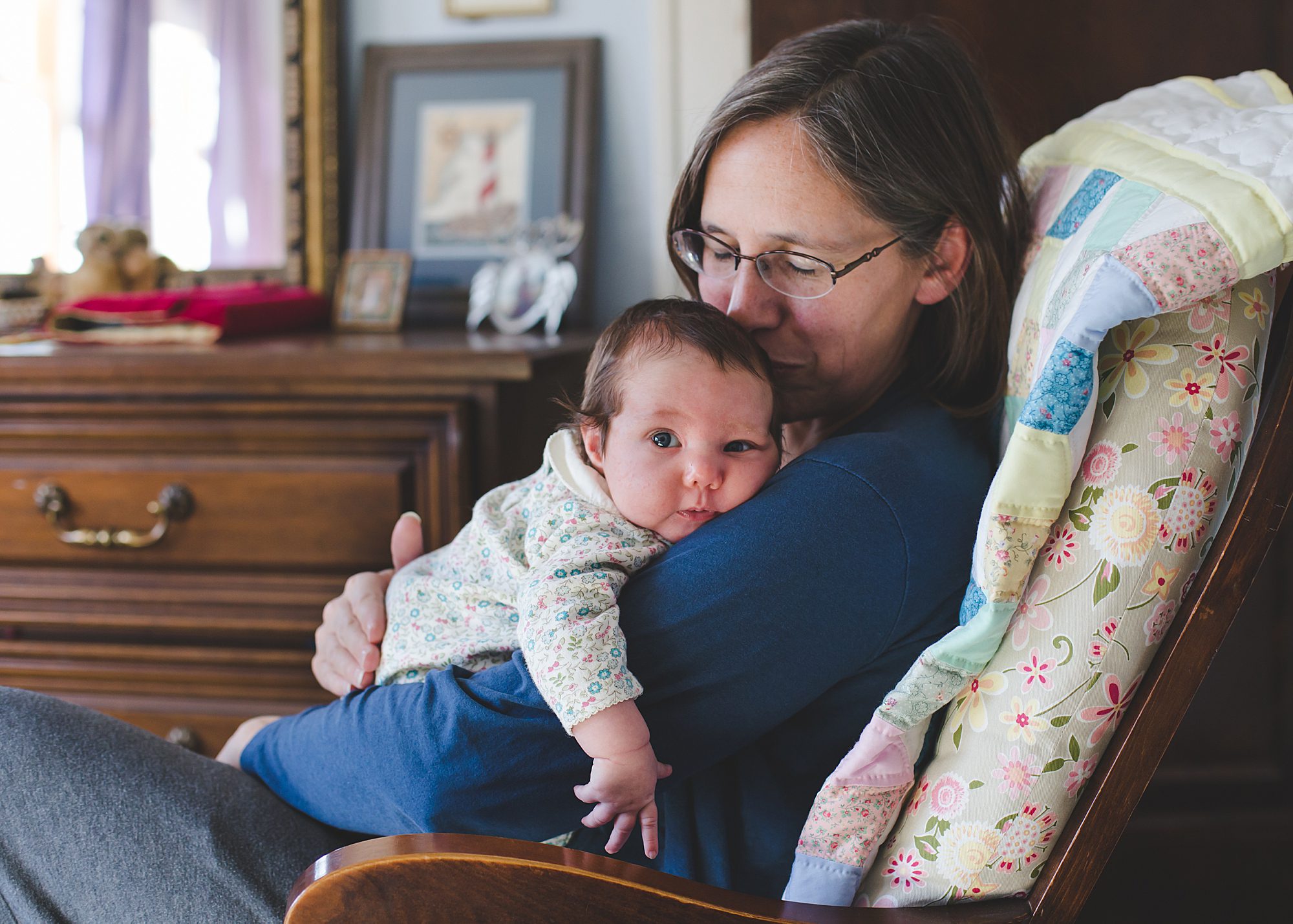 A mom kissing and holding a baby in rocking chair.
