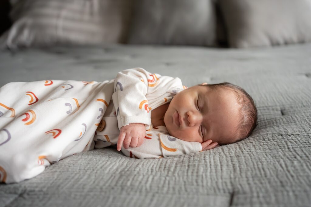 A baby sleeping on a bed with a rainbow swaddle.