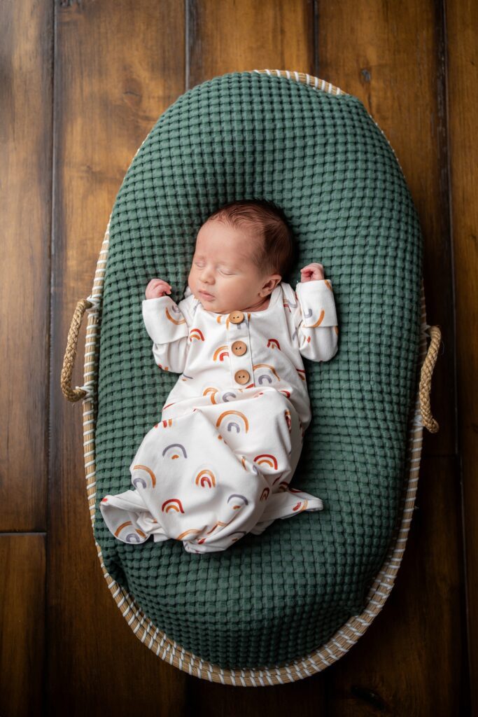 A baby sleeping in a green basket on a wooden floor.