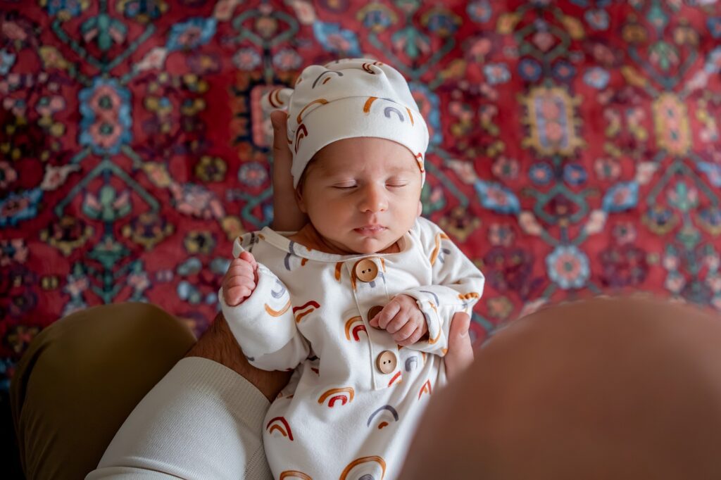 A baby is wearing a hat and sitting on a rug.