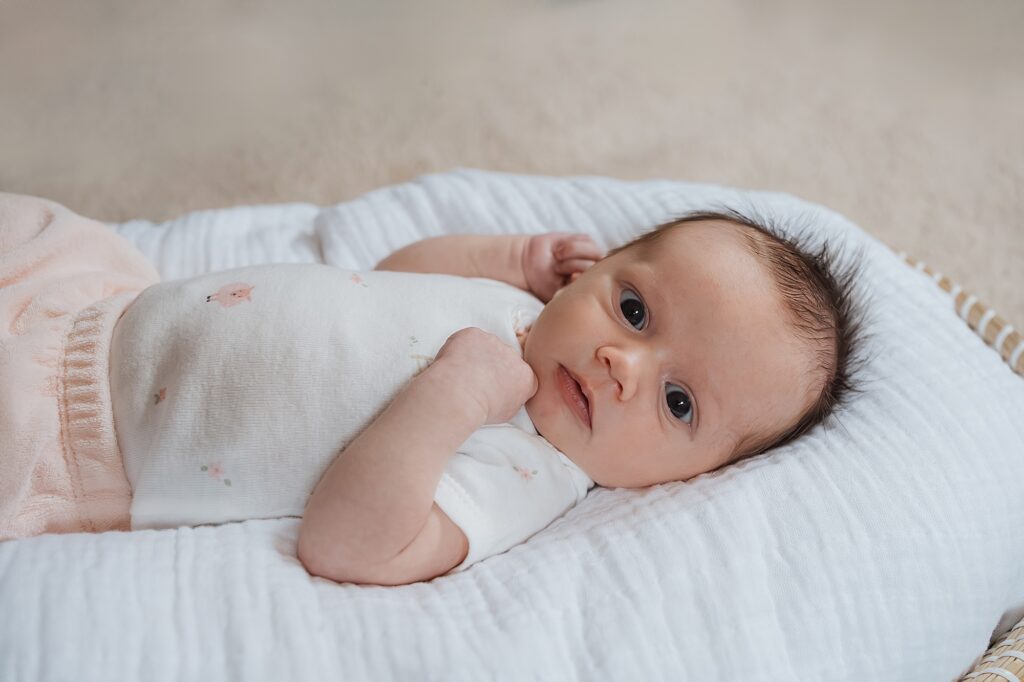A newborn photographer captures an alert infant lying comfortably on a soft surface, dressed in a pastel outfit with floral accents.