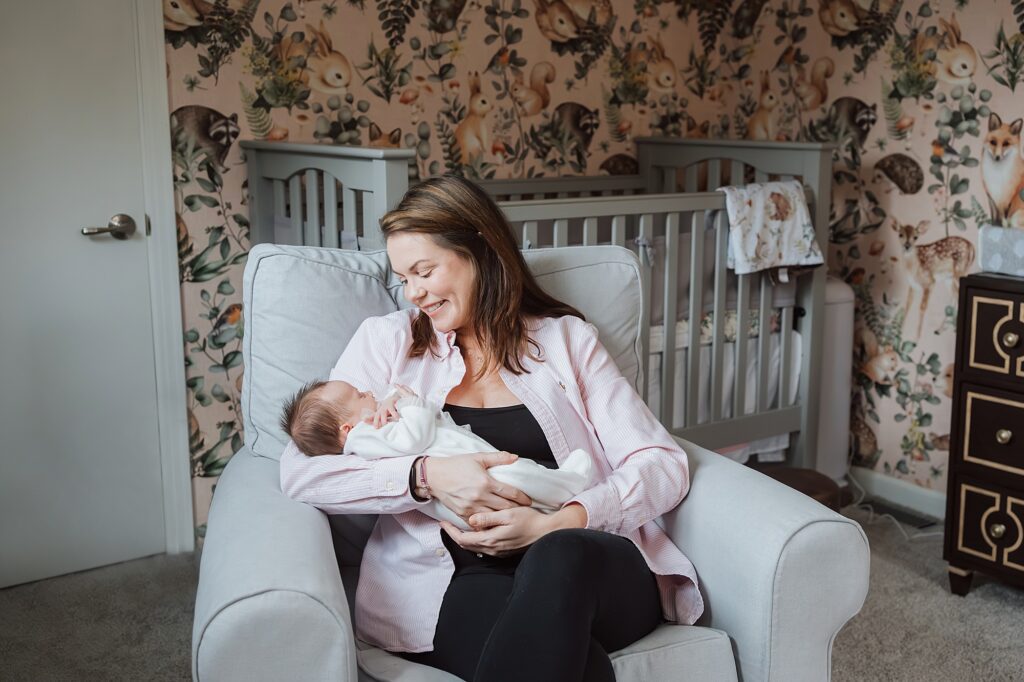 A newborn photographer capturing a woman sitting in a rocking chair, tenderly holding a sleeping baby in a nursery.