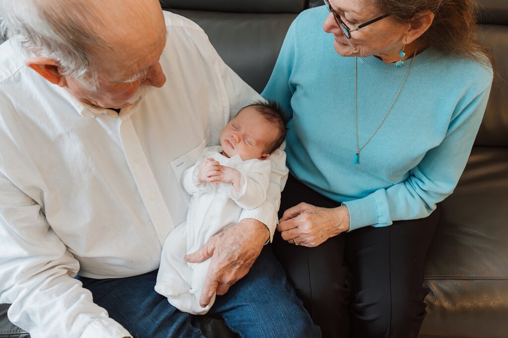 Elderly couple enjoying a moment with their newborn grandchild and their newborn photographer.