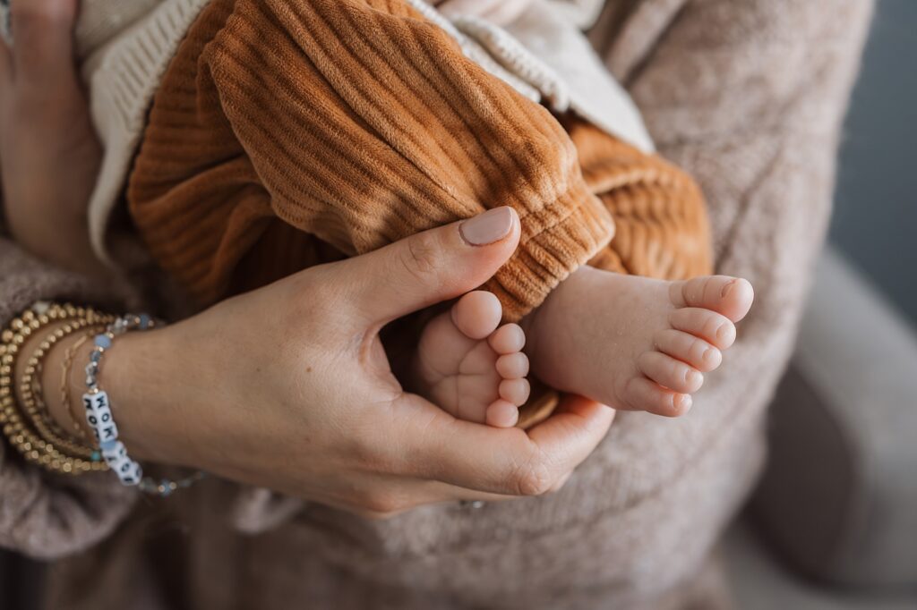 A close-up photo capturing a baby's bare feet cradled gently in an adult's hands, with the baby wearing orange pants.