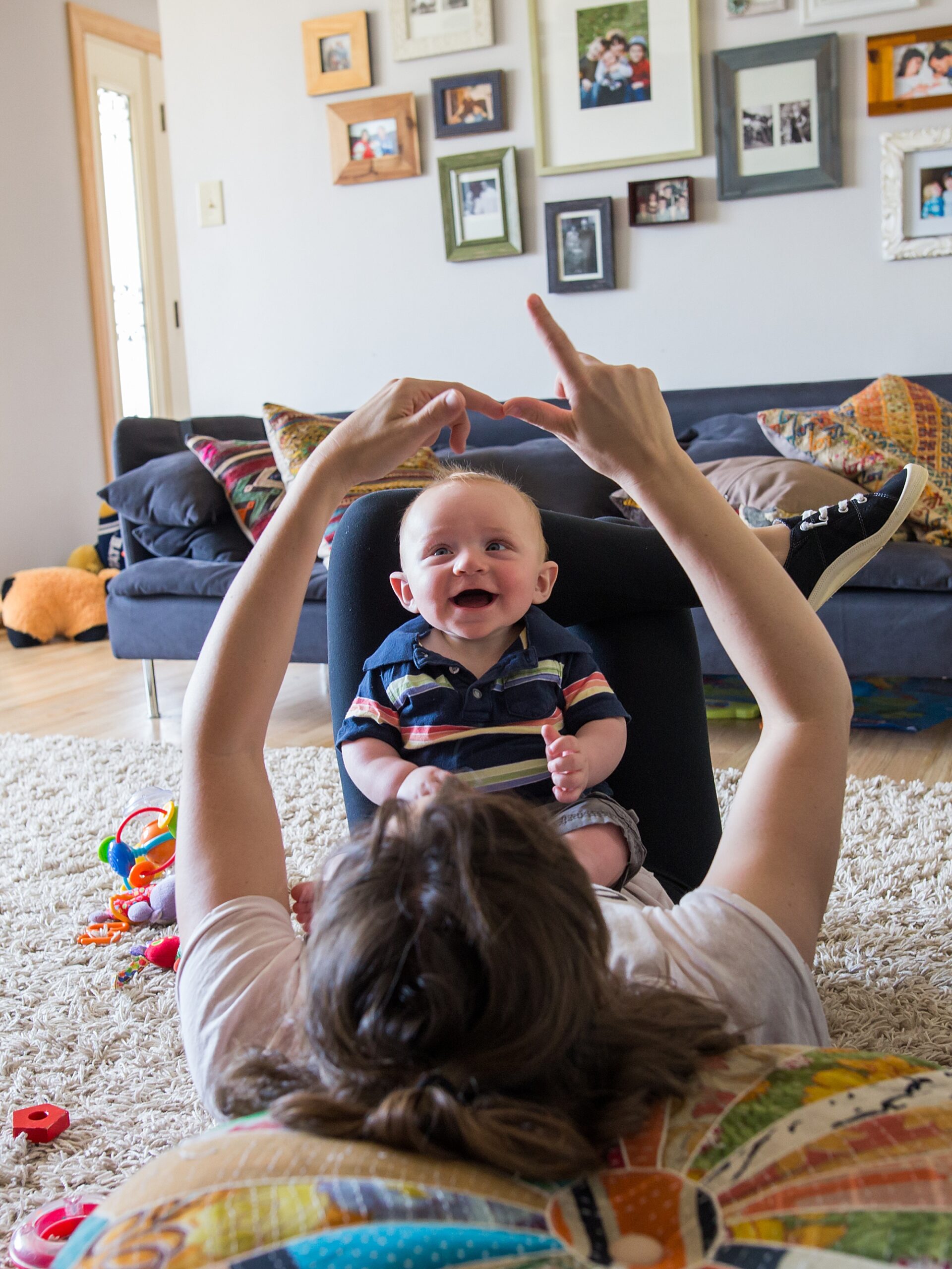 A baby smiles joyfully while playing with an adult lying on the floor, who is lifting the baby up with their feet.