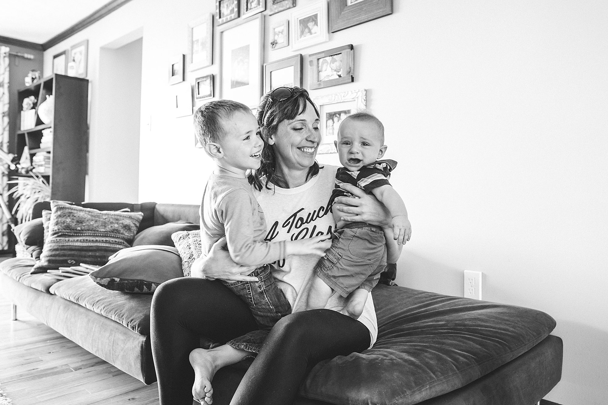 A woman sitting on a couch with two young children, smiling and embracing them.