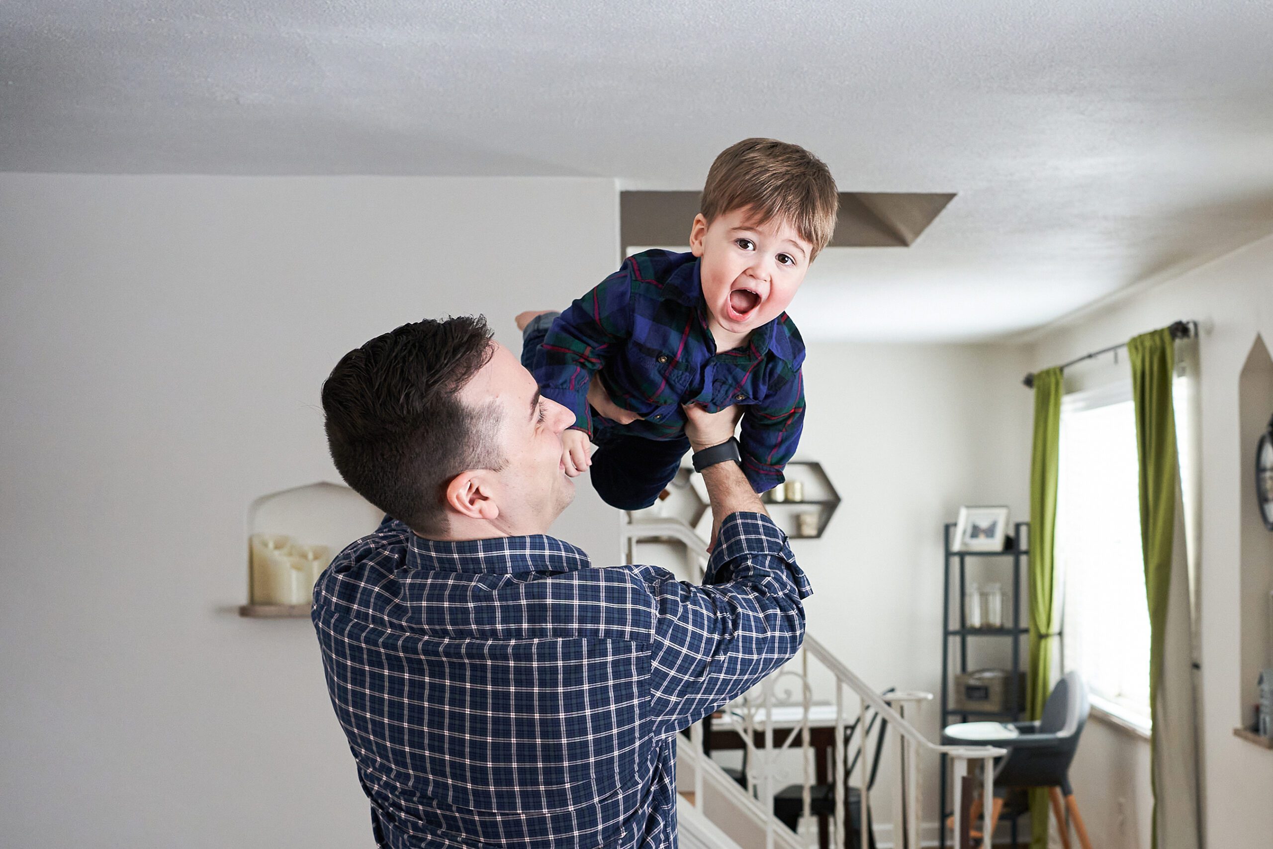 A man lifting a cheerful child in the air inside a home.