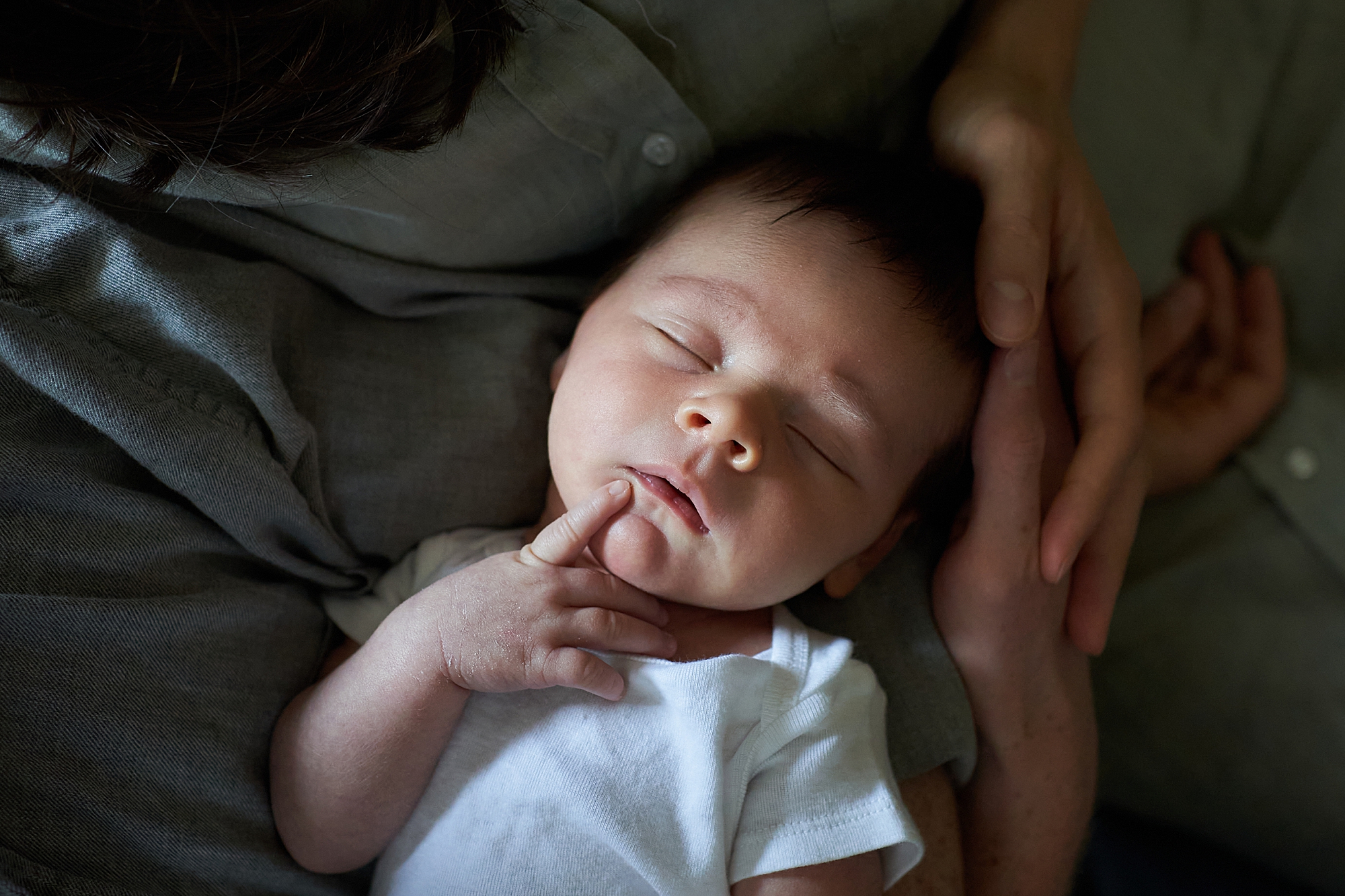 A newborn baby sleeping peacefully on an adult's chest with a hand gently resting on the baby's head.