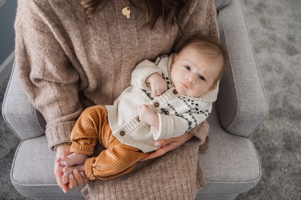 A woman cradling an infant in a cozy knitted outfit.