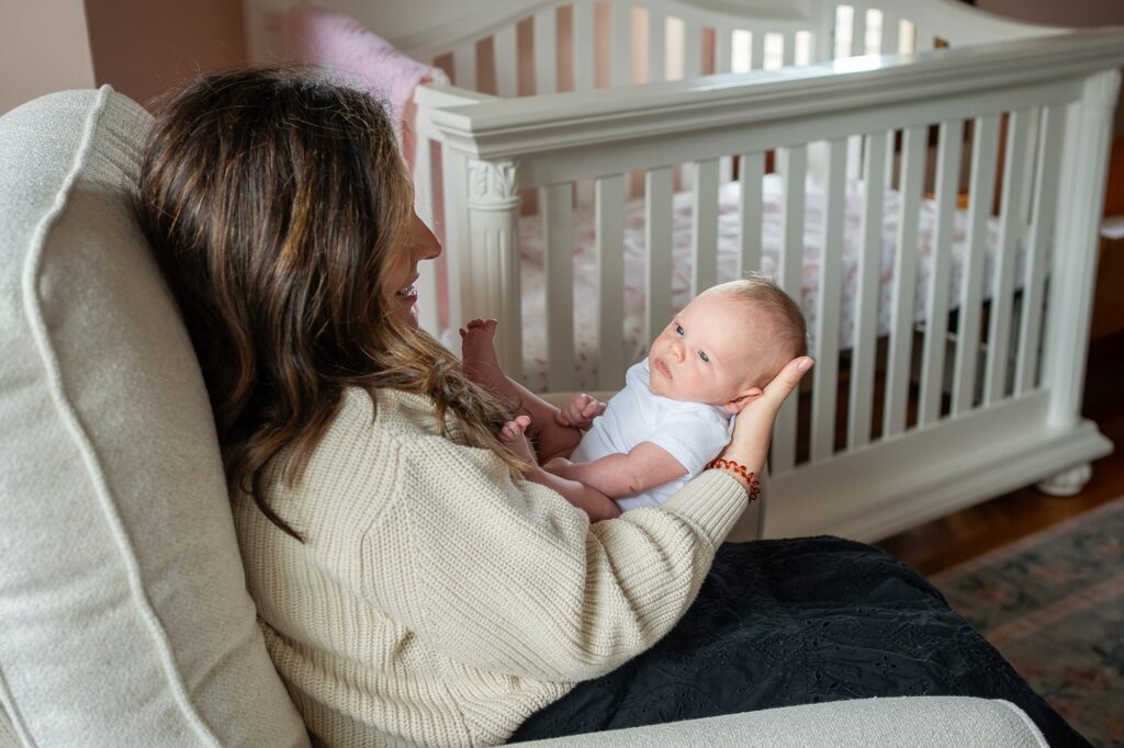 A mother holding her baby in a nursery while sitting in a rocking chair.