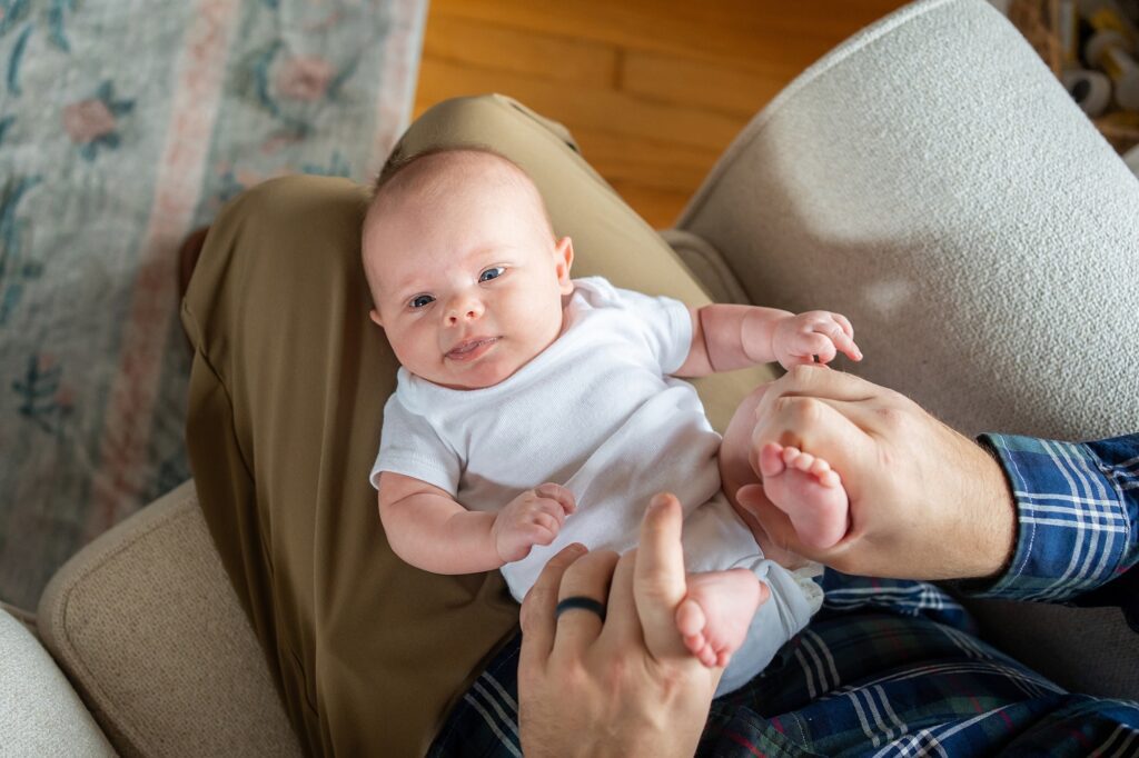 An infant resting on an adult's lap, looking curiously towards the camera.