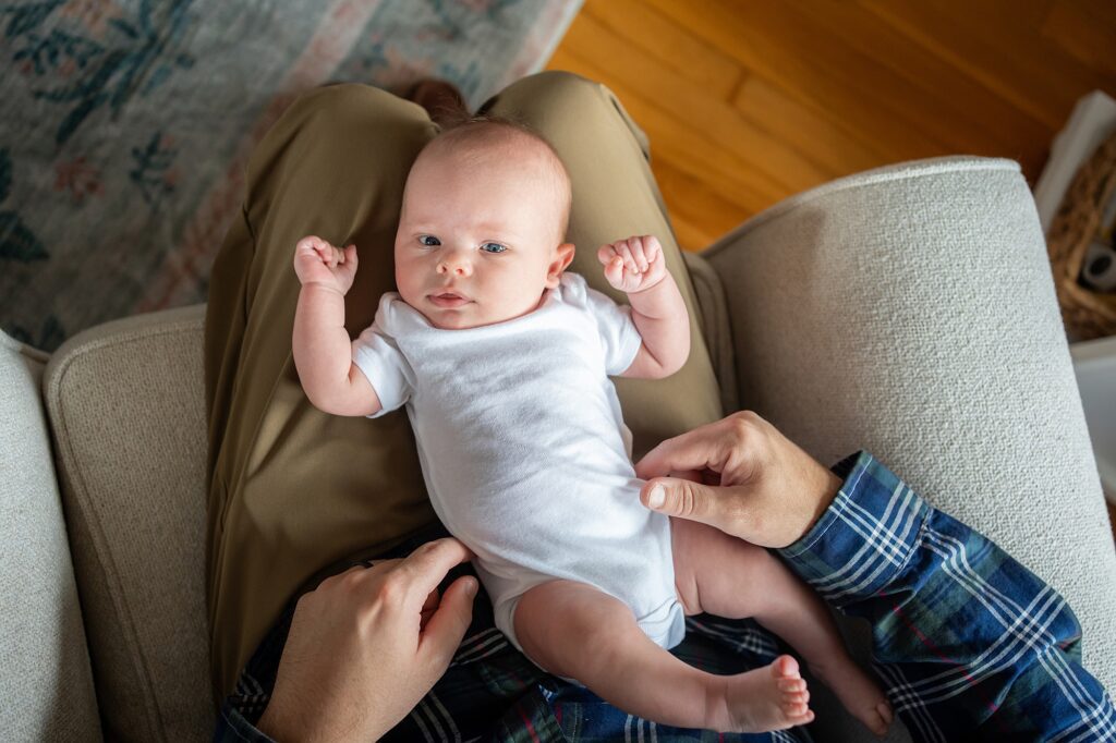 An infant lying on an adult's lap, looking directly at the camera.