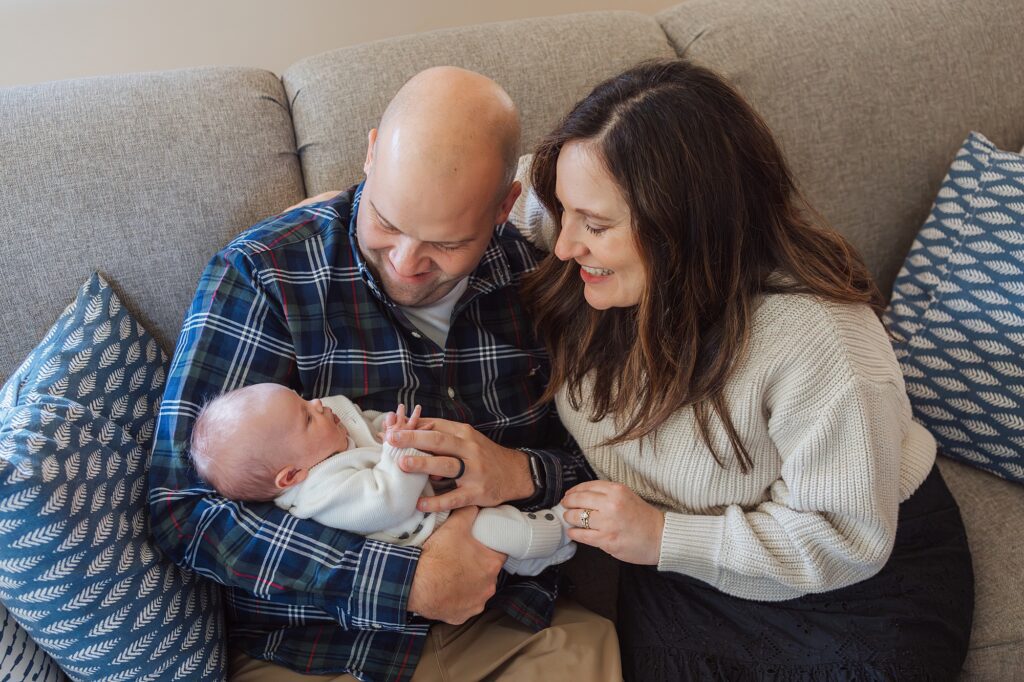 A couple adoring their baby while sitting on a couch.
