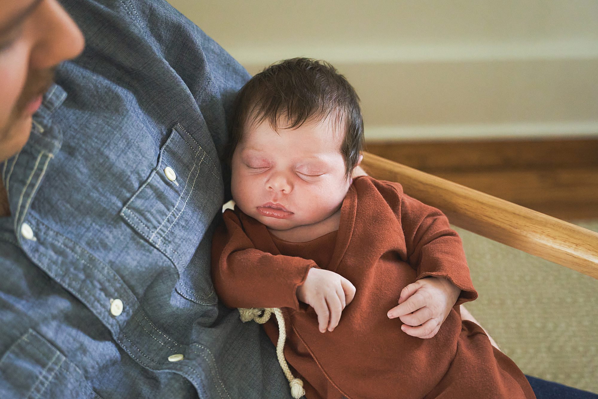 Newborn sleeping peacefully against an adult's chest.