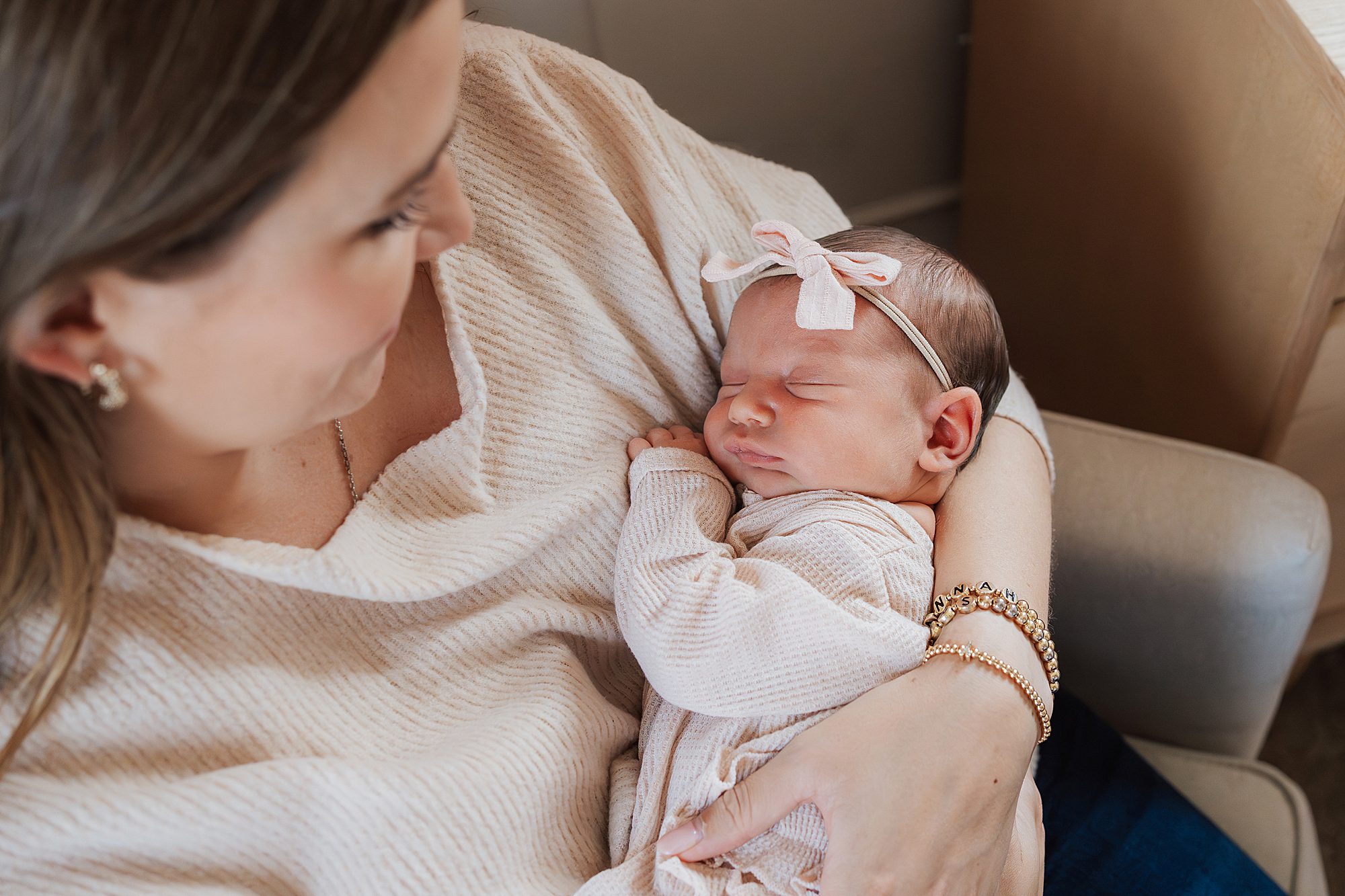 mother holding a sleeping newborn adorned with a bow headband.
