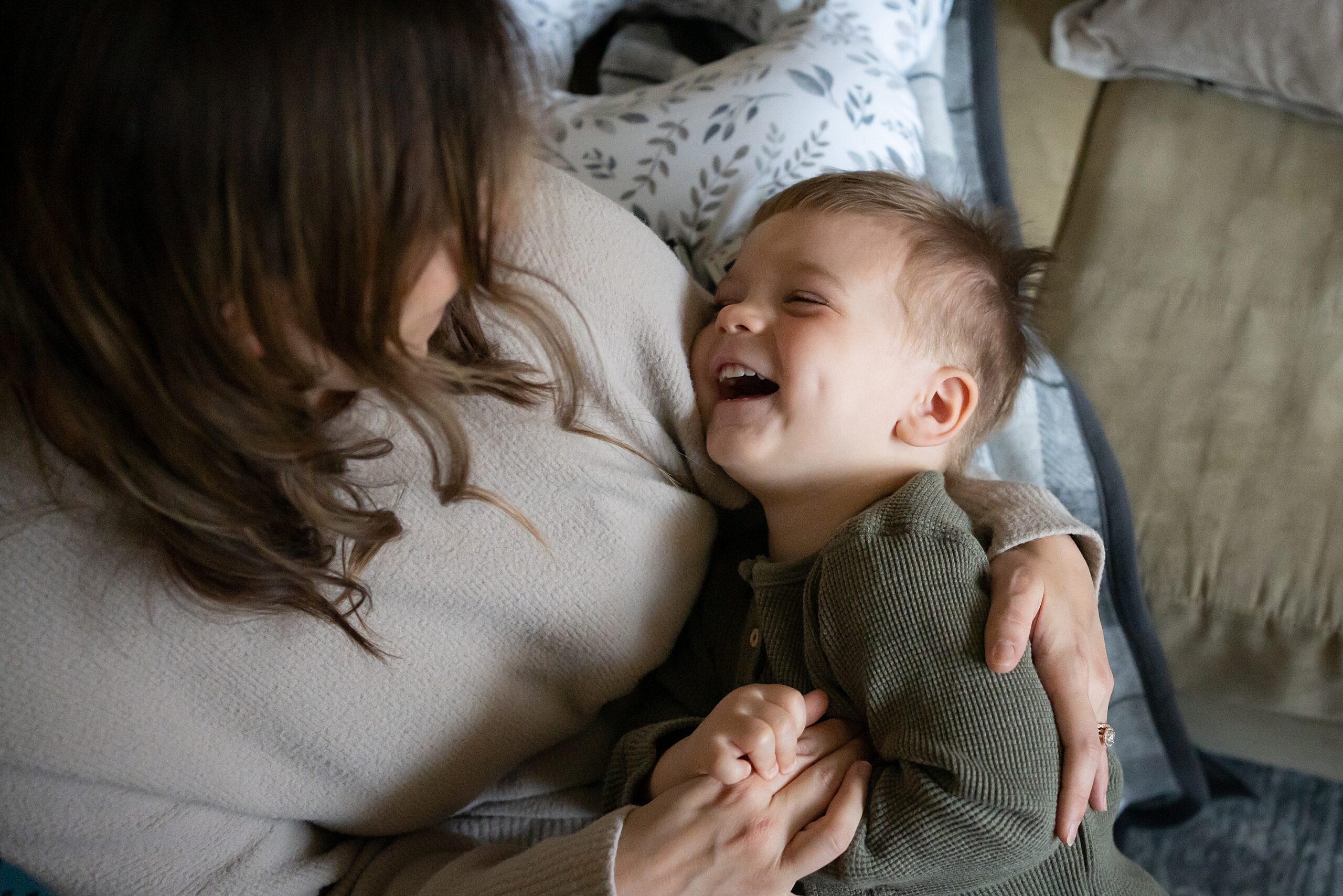 A joyful toddler laughing in the embrace of an adult, most likely their mother, in a cozy indoor setting.