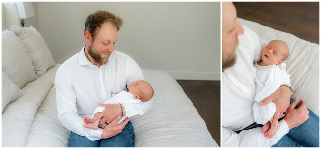 A man with a beard in a white shirt sitting on a couch, holding and looking at a newborn baby with affection.