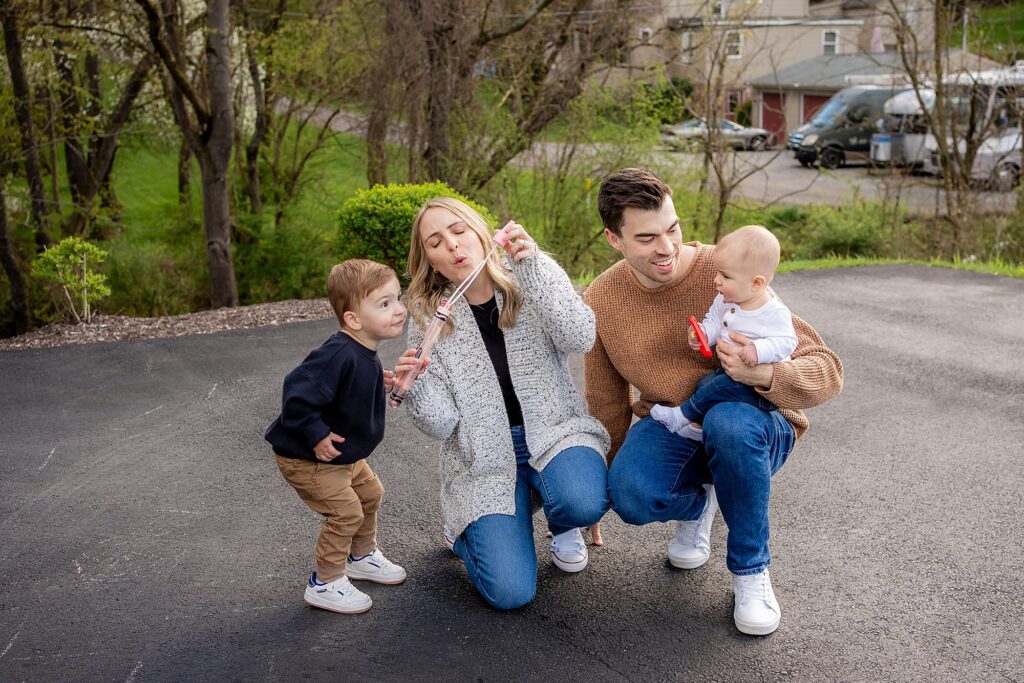 A family of four, with two young children, enjoys making bubbles together on a sunny day outdoors.