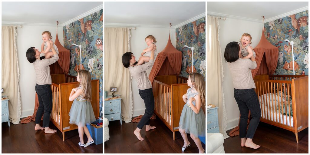A woman lifts a baby out of a crib while a young girl stands nearby. The room is decorated with animal-themed wallpaper and a canopy above the crib.