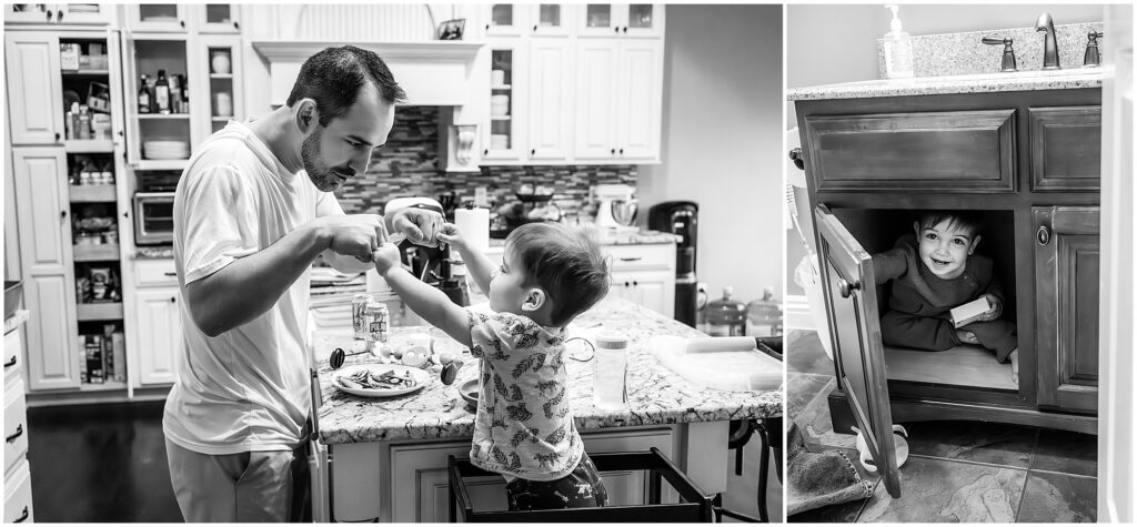 Father helps child with toothbrush at kitchen counter; another child peeks from under-sink cabinet in black and white kitchen setting.